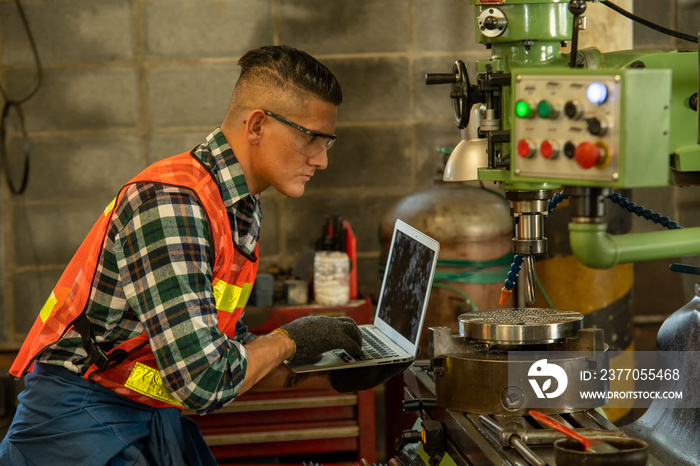 Mechanical engineer wearing safety harness use laptop with milling machine at factory.