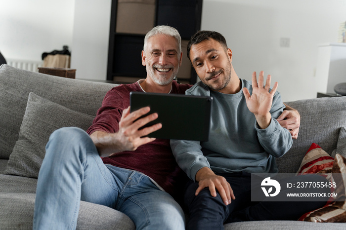 Smiling male couple taking selfie on sofa