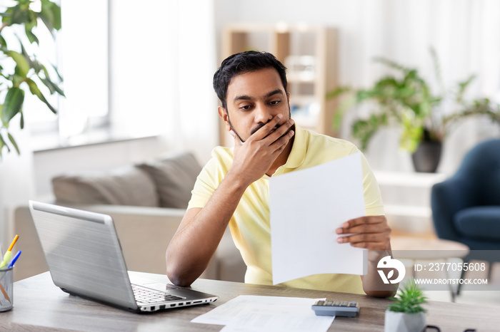 remote job, technology and people concept - stressed young indian man with calculator and papers working at home office