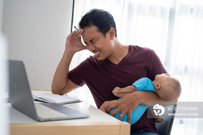 portrait of a stress busy father working from home while holding his infant baby