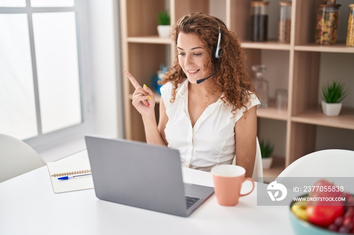 Young caucasian woman wearing call center agent headset working from home smiling happy pointing with hand and finger to the side