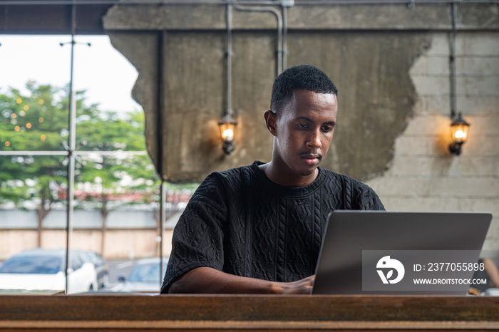 Handsome black man sitting and using laptop computer indoors