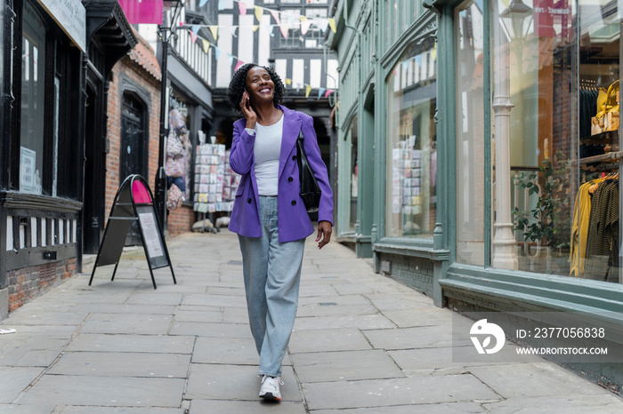 Smiling woman talking by smart phone while walking in city