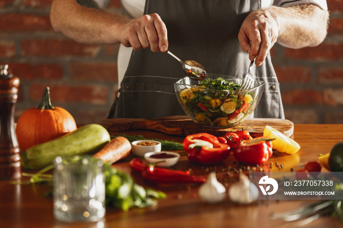 Close-up hands of male chef, cook preparing fresh vegetable salad in his cafe, restaurant kitchen. Concept of a correct, healthy diet.