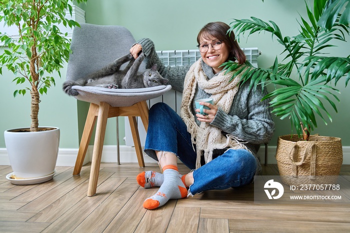 Cold winter season, woman with cat on chair near heating radiator