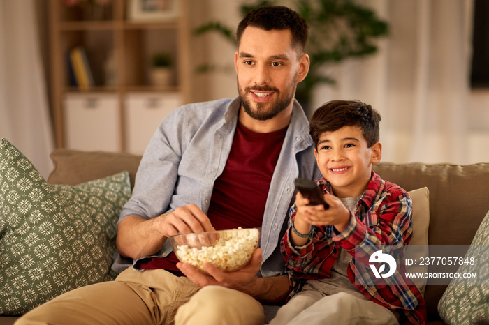 family, childhood, fatherhood, technology and people concept - happy father and little son with popcorn watching tv at home in evening