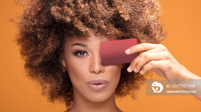 Young afro girl holding credit card on yellow background.