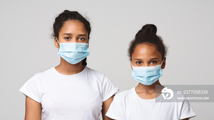 Two young sisters wearing medical masks over grey studio background