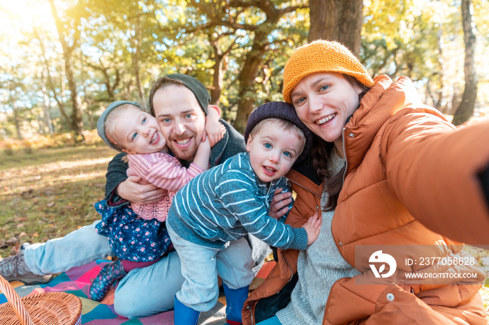 Happy family taking a selfie together on a sunny autumn day - Mother and father holding their daughter and son and having fun all together in a cute group hug