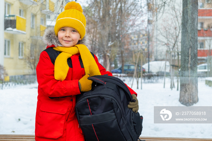 Boy with backpack sits at bus stop and waits for bus in winter.