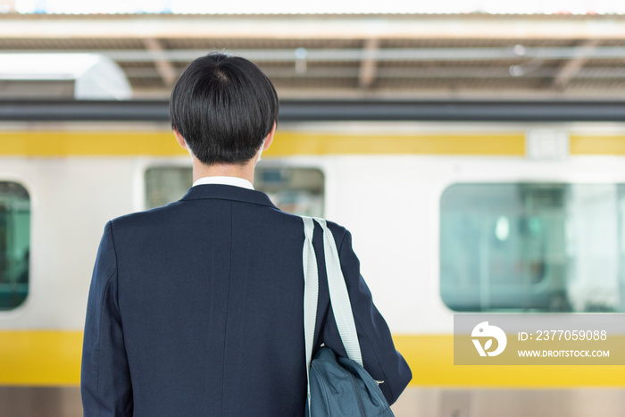 駅のホームで電車を待つ男子高校生