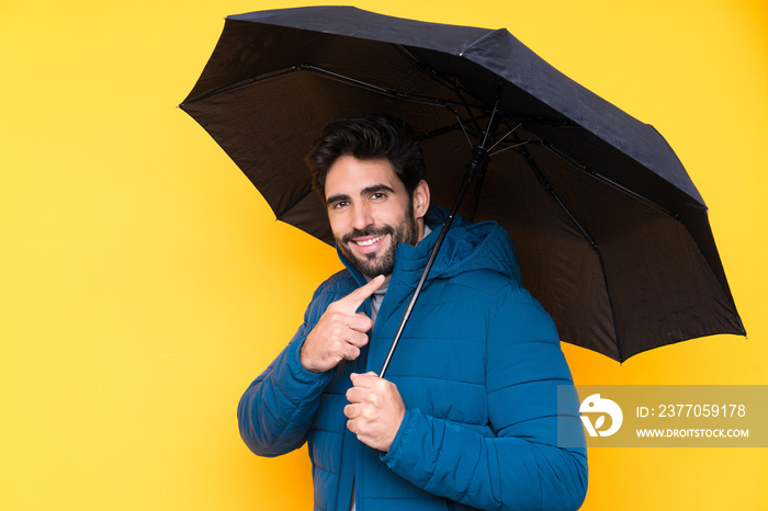 Man holding an umbrella over isolated yellow background and pointing it