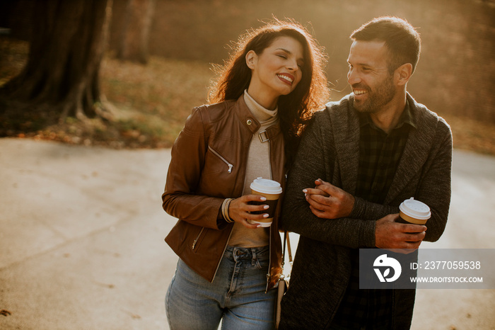 Young couple walking in autumn park with coffee to go cups in hands