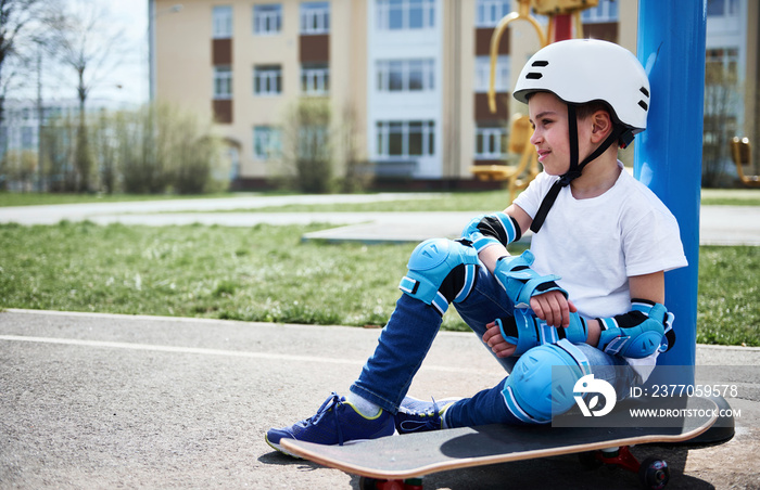 Cute child boy relaxed sitting on skateboard against yellow building background