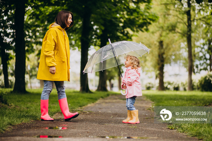 Mother with daughter walking in the rain under the umbrella