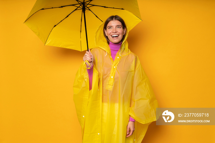 woman in yellow waterproof raincoat with umbrella checking for rain standing under parasol