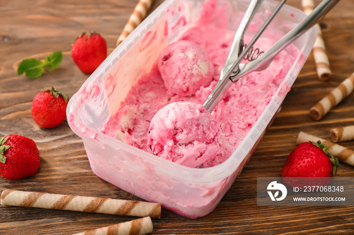 Container with delicious strawberry ice-cream and wafer sticks on wooden background, closeup