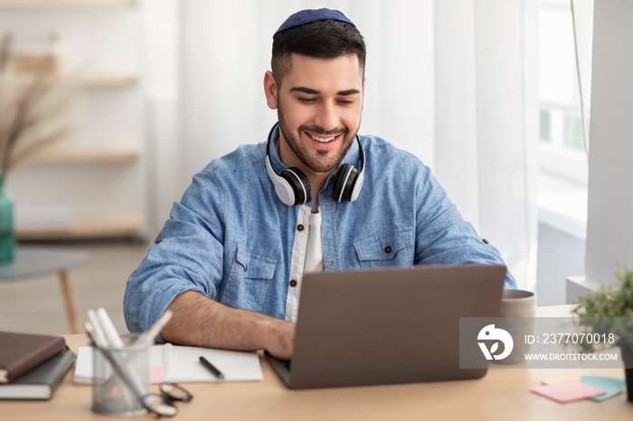 Smiling israeli man working on laptop at home