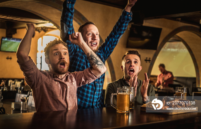 Friends drinking draft beer and watching tv in a pub