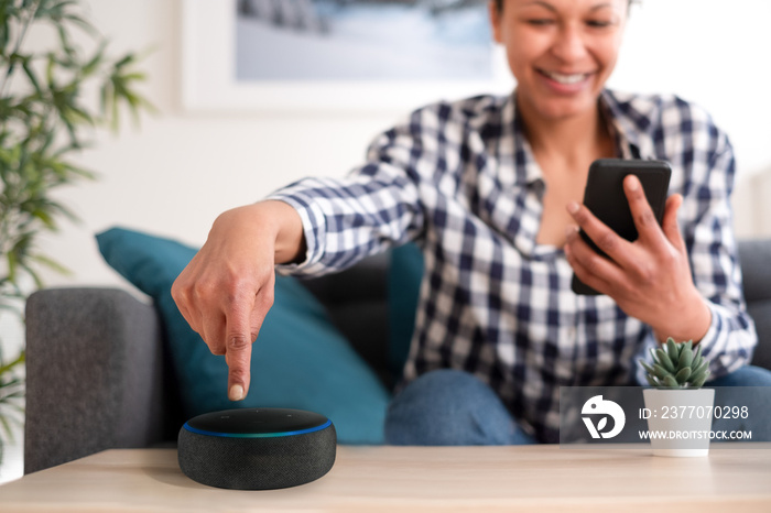 Black woman connecting phone to her virtual assistant smart speaker