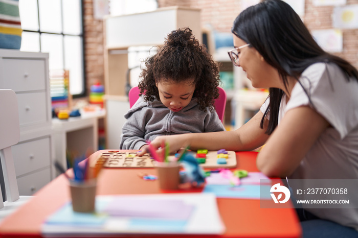 Teacher and toddler playing with maths puzzle game sitting on table at kindergarten