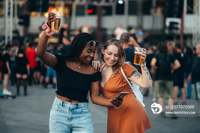 Friends using smartphone and drinking beer on a music festival