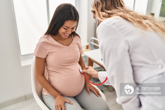 Young latin woman pregnant and doctor auscultating belly at clinic