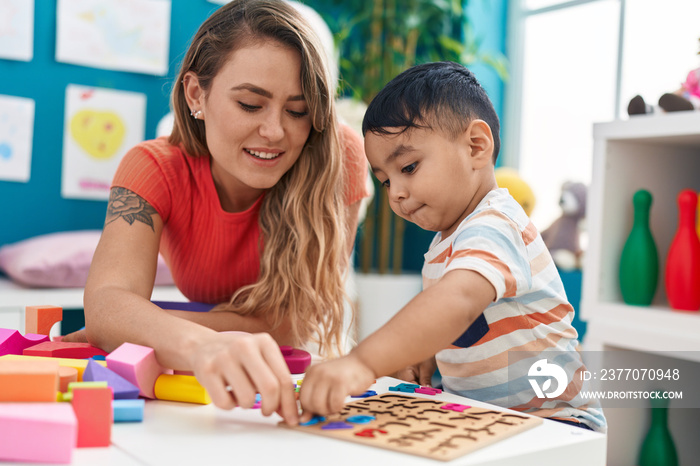 Teacher and toddler playing with maths puzzle game sitting on table at kindergarten