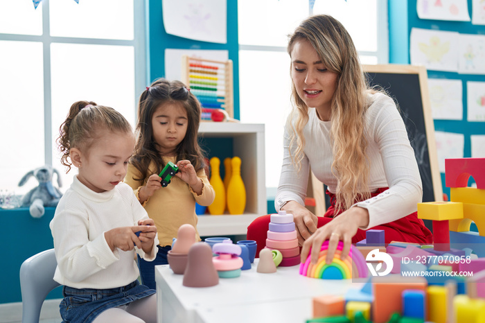 Teacher with girls playing with geometry blocks sitting on table at kindergarten