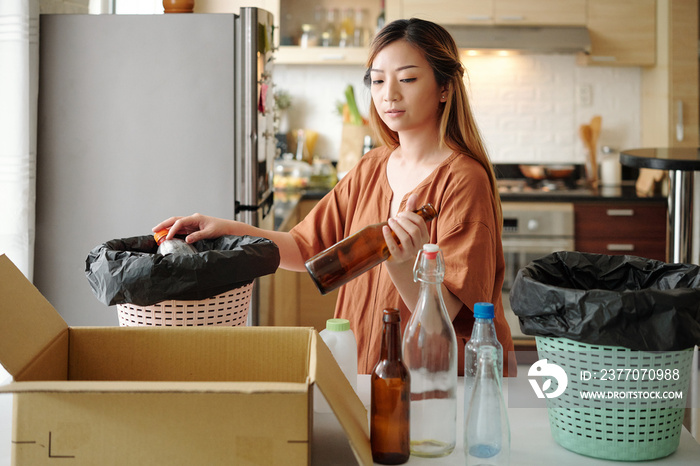 Young woman sorting waste and grouping into different categories at her kitchen table