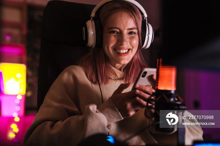 Image of cheerful girl using mobile phone while playing video game