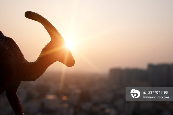 silhouette of parasaurolophus and buildings in sunset time