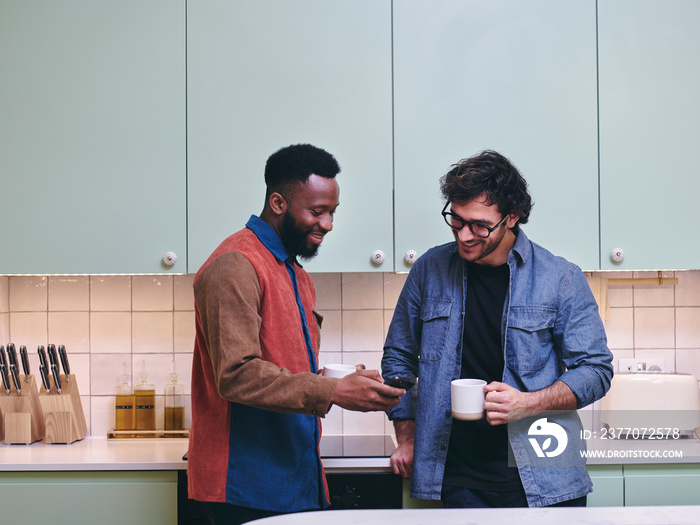 UK, London, Two smiling men looking at smart phone in kitchen