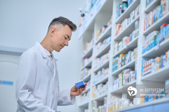 Pleased man in lab coat reviewing medications at pharmacy