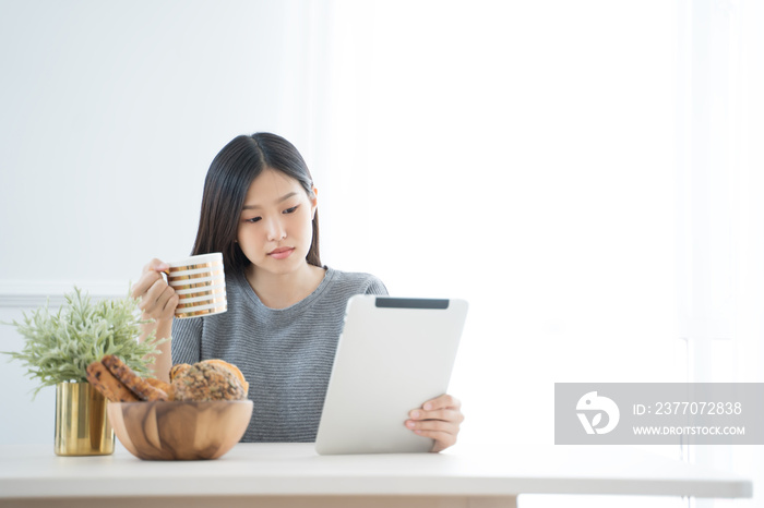 Young Asian woman using tablet at home and having breakfast in the morning .She reading on tablet.