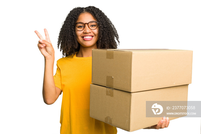 Young african american woman moving to other house while picking up a box full of things isolated joyful and carefree showing a peace symbol with fingers.