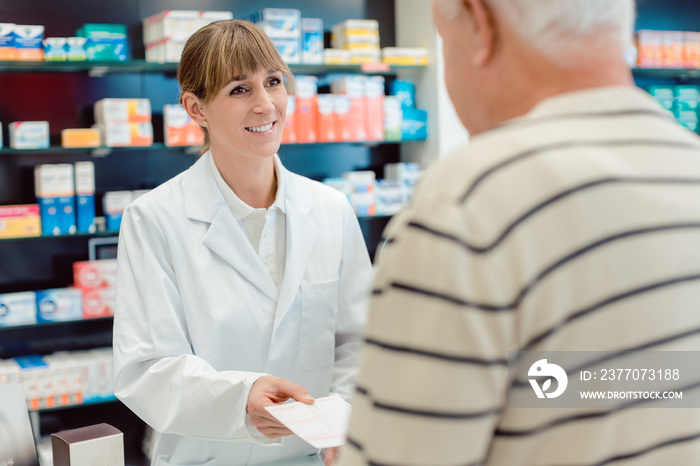 Pharmacist taking prescription slip from senior man