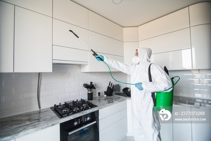 Disinfector in a protective suit conducts disinfection in contaminated area. Professional disinfection against COVID-19, coronavirus. in clothing protecting from chemical poisoning in the kitchen