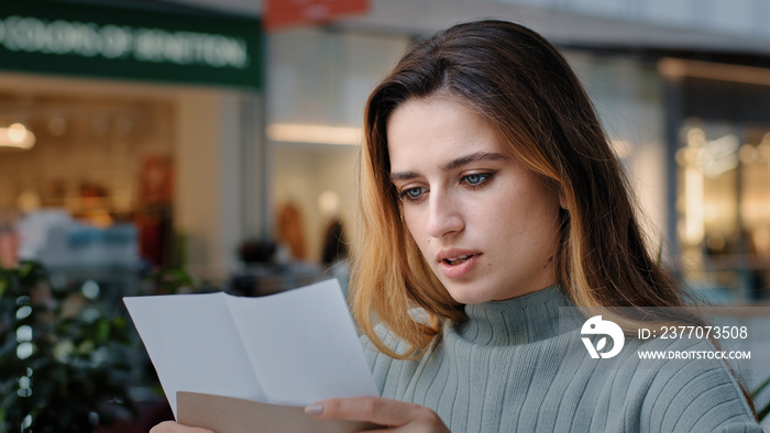 Portrait of beautiful young caucasian millennial woman recipient girl sitting in cafe receiving letter opens envelope reads test results bank notice news from friends new job offer insurance statement