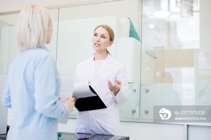 Confident pharmacy manager in whitecoat consulting one of clients about new medicine