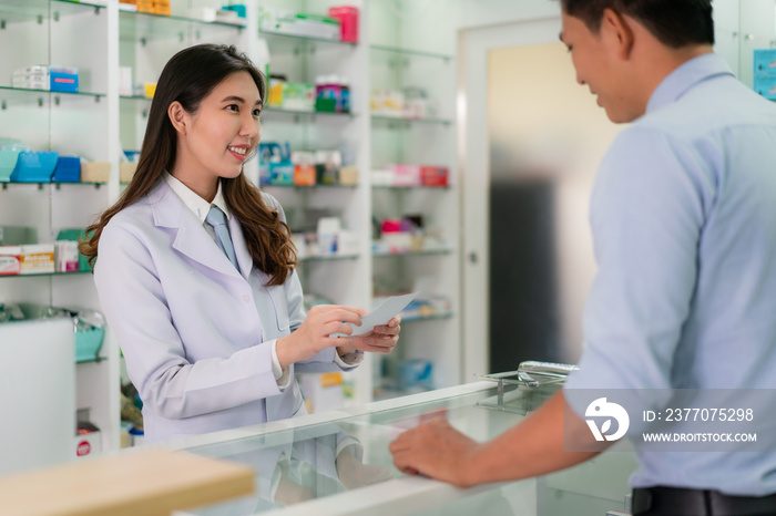 Confident Asian young female pharmacist with a lovely friendly smile and receive medicine prescription from man patient in the pharmacy drugstore. Medicine, pharmaceutics, health care concept.