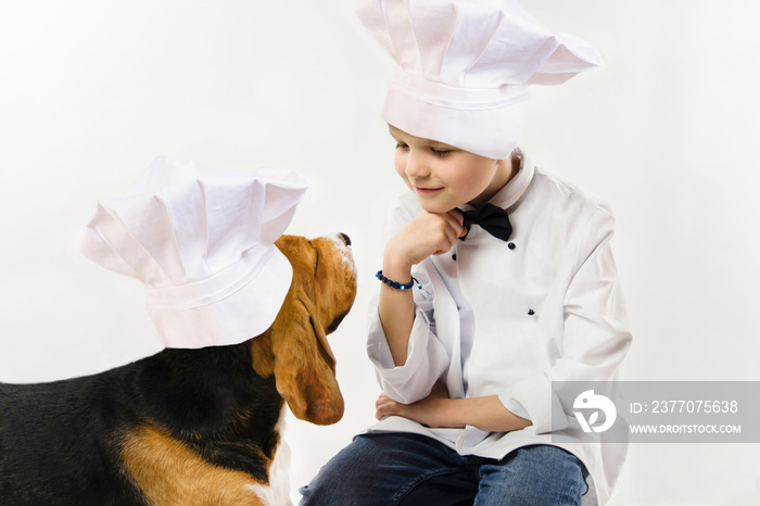 funny boy in chef uniform and cute beagle dog in chef’s cap cook dinner