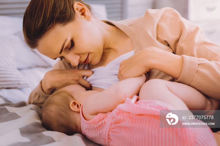 Hungry baby. Relaxed young woman breastfeeding her baby daughter while staying at home during her maternity leave