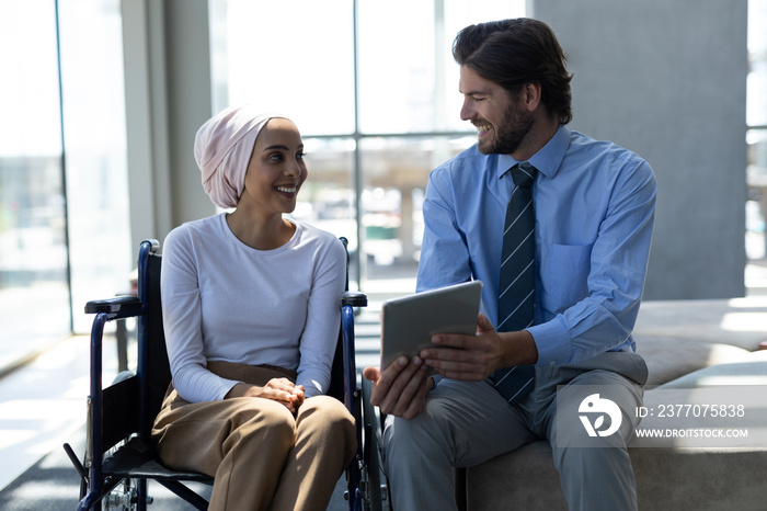 Happy disabled mixed-race female executive with Caucasian businessman discussing over digital tablet