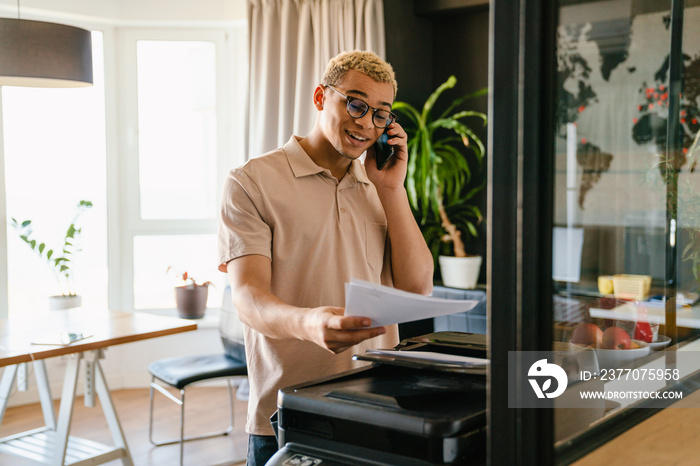 African business man using printer while talking on mobile phone in office