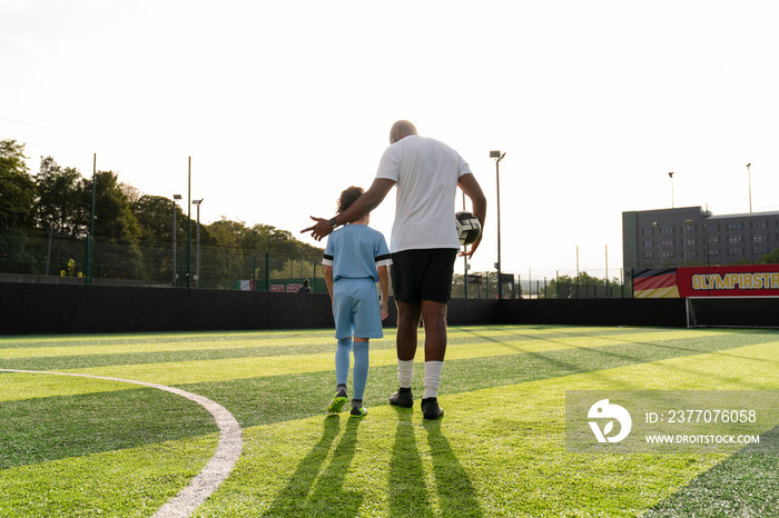 Rear view of coach and girl (6-7) on soccer field