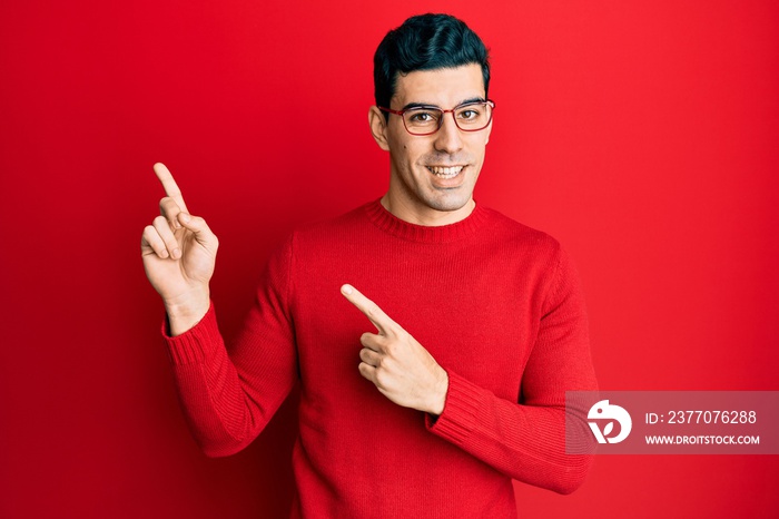 Handsome hispanic man wearing casual clothes and glasses smiling and looking at the camera pointing with two hands and fingers to the side.