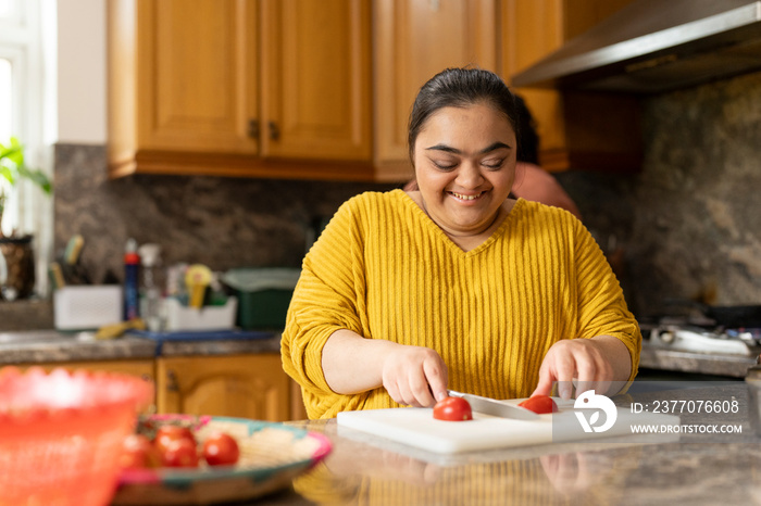 Smiling woman with down syndrome cutting tomato in kitchen