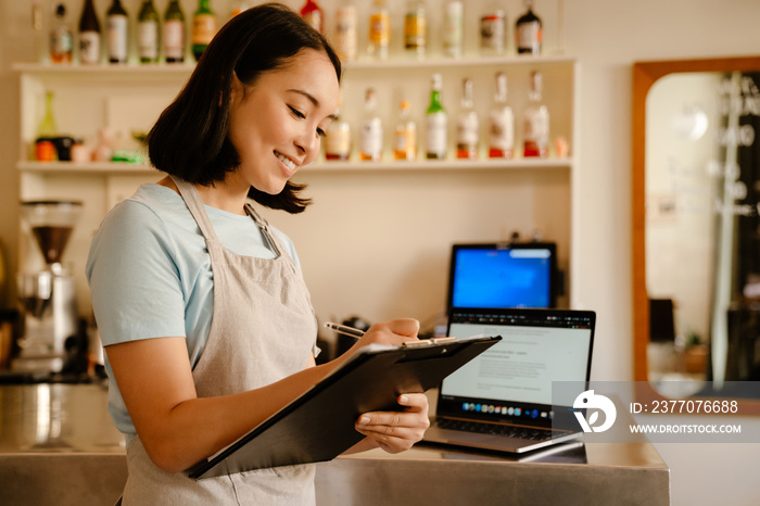 Asian barista woman writing down notes while working in cafe