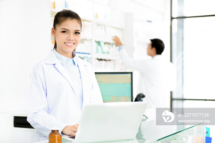 Young smiling Asian female pharmacist working in chemist shop or pharmacy